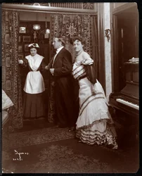 Formalnie ubrany mężczyzna i kobieta oraz coś, co wygląda na służącego w pokoju z fortepianem, 1905 (srebrny odbitka żelatynowa)
